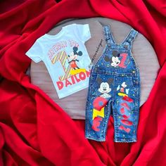 two children's clothing items laying on top of a red blanket