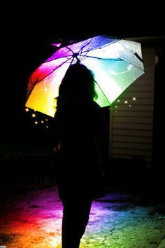 a woman standing in the dark holding an umbrella with colored lights shining on her face