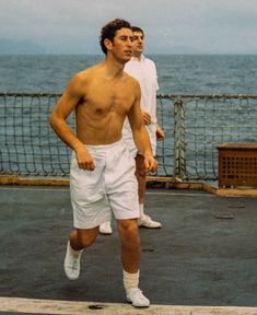 two men are running on the deck of an ocean ship, one is shirtless