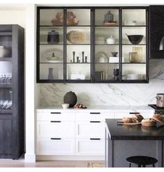 a kitchen with black cabinets and marble counter tops, along with white cupboards that have glass doors