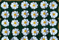 a crocheted granny blanket with white and yellow flowers on the center is laying on a wooden surface