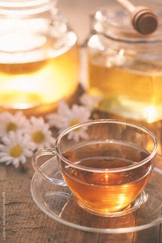 a glass cup filled with tea sitting on top of a wooden table next to jars of honey