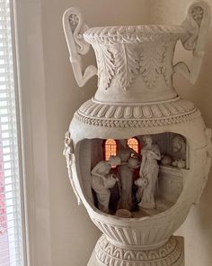 a white vase sitting on top of a table next to a window