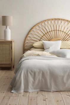 a bed with white linens and pillows in a bedroom setting, next to a wicker night stand