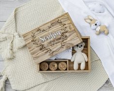 a wooden box with two small stuffed animals in it next to some other items on a white blanket