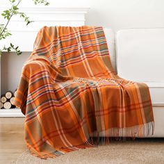 an orange plaid blanket sitting on top of a white couch next to a potted plant