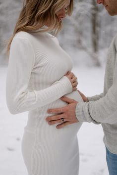 a pregnant woman is holding her husband's belly in the snow while they are looking at each other