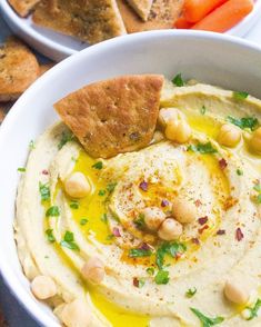 hummus with pita chips, carrots and crackers on the side in white bowls