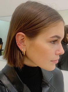 a woman in a black leather jacket is wearing gold hoop earrings and a black turtle neck sweater