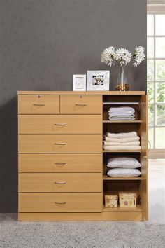 an open cabinet with folded towels and flowers on top in front of a gray wall