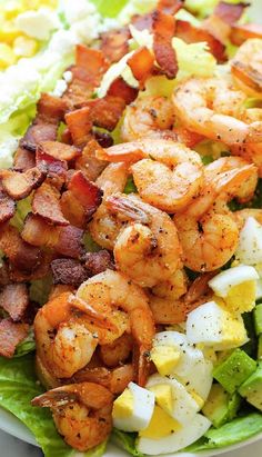 a salad with shrimp, avocado and bacon on it is sitting on a marble surface