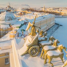 statues of horses and carriages in the snow on top of a building with buildings in the background