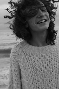 a woman standing on the beach with her hair blowing in the wind and smiling at the camera