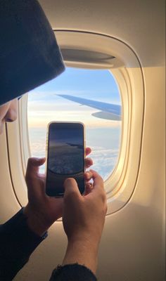 a person is looking at their cell phone while flying in the sky with an airplane window