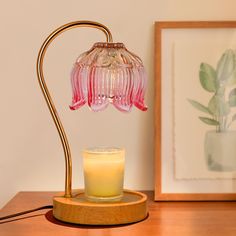 a pink glass lamp sitting on top of a wooden table next to a lit candle