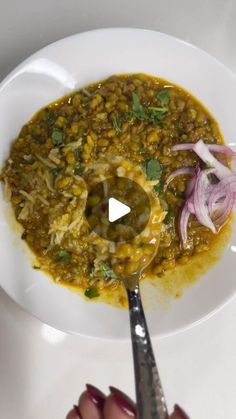 a white plate topped with green lentils and red onions next to a silver spoon