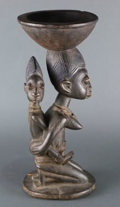 an old bronze vase with two heads on it's legs and one sitting in front of the bowl