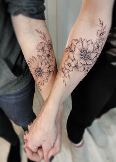 two people holding hands with tattoos on their arms and the other hand is covered by flowers