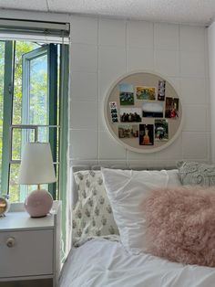 a white bed topped with pillows next to a window covered in pictures and pink throw pillows