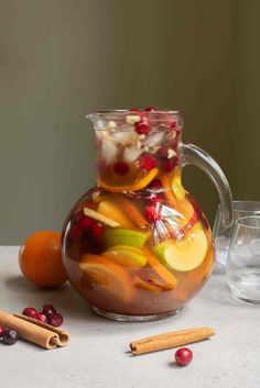 a pitcher filled with liquid next to oranges and cranberries