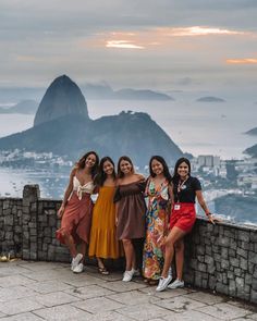 four women posing for a photo in front of the ocean with mountains and buildings in the background