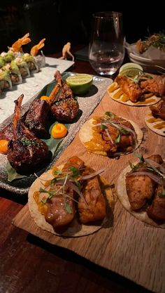 a wooden table topped with different types of food and plates filled with meat, veggies and dipping sauces