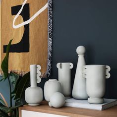 some white vases are sitting on top of a dresser in front of a painting