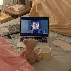 a teddy bear sitting in front of a laptop on a bed with pillows and blankets