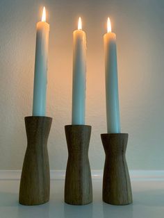 three wooden candlesticks with one lit and the other turned on, in front of a white wall