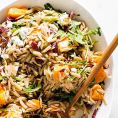 a white bowl filled with pasta salad next to a wooden spoon on top of a table