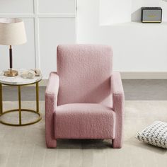 a pink chair sitting next to a table with a lamp on it's side