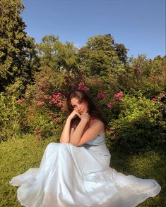 a woman in a white dress sitting on the ground with her hand under her chin