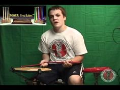 a young man sitting in front of a green screen holding two drums and drumming sticks