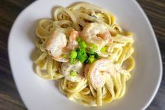 a white plate topped with pasta covered in shrimp and peas on top of a wooden table