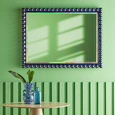 a green room with a table, vase and mirror on the wall in front of it