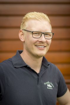 a man with glasses is smiling for the camera while standing in front of a wooden wall