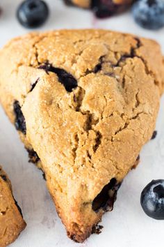 a blueberry muffin is cut in half on a white surface with fresh blueberries around it