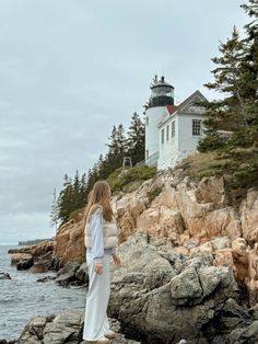 a woman standing on rocks near the ocean with a light house in the back ground