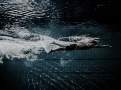 a man is swimming in the water with his back to the camera and head down