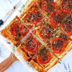 a square pizza with tomatoes and herbs cut into squares on a cutting board next to a knife