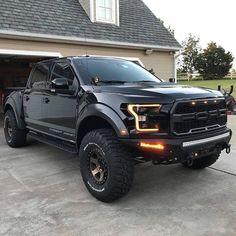 a large black truck parked in front of a garage with its lights on and the door open