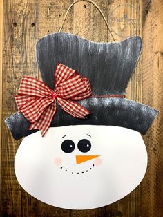 a paper plate snowman with a red bow on it's head is hanging from a wooden wall