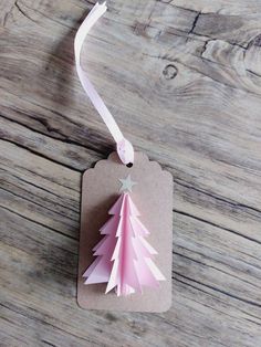 a pink christmas tree ornament hanging from a white ribbon on a wooden table