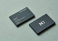 two black business cards sitting on top of a gray table next to an orange cell phone