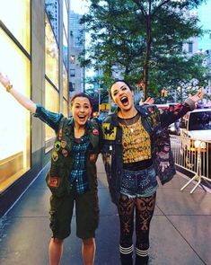 two women standing on the sidewalk with their arms in the air