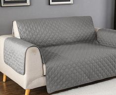 a couch covered in a gray quilted cover next to two pictures on the wall