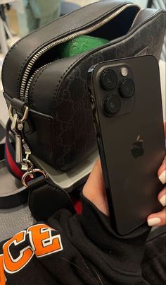 a person holding an iphone in front of a black bag and some other items on a table