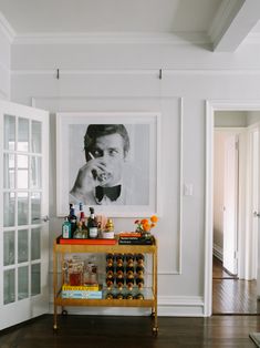 a bar cart with liquor bottles on it in front of a framed photo and wooden floors