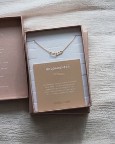 an open box with a necklace in it on top of a white bed sheet next to a card that says goddaughter