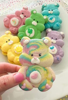 a person holding a small teddy bear in front of some colorful cookies on a plate